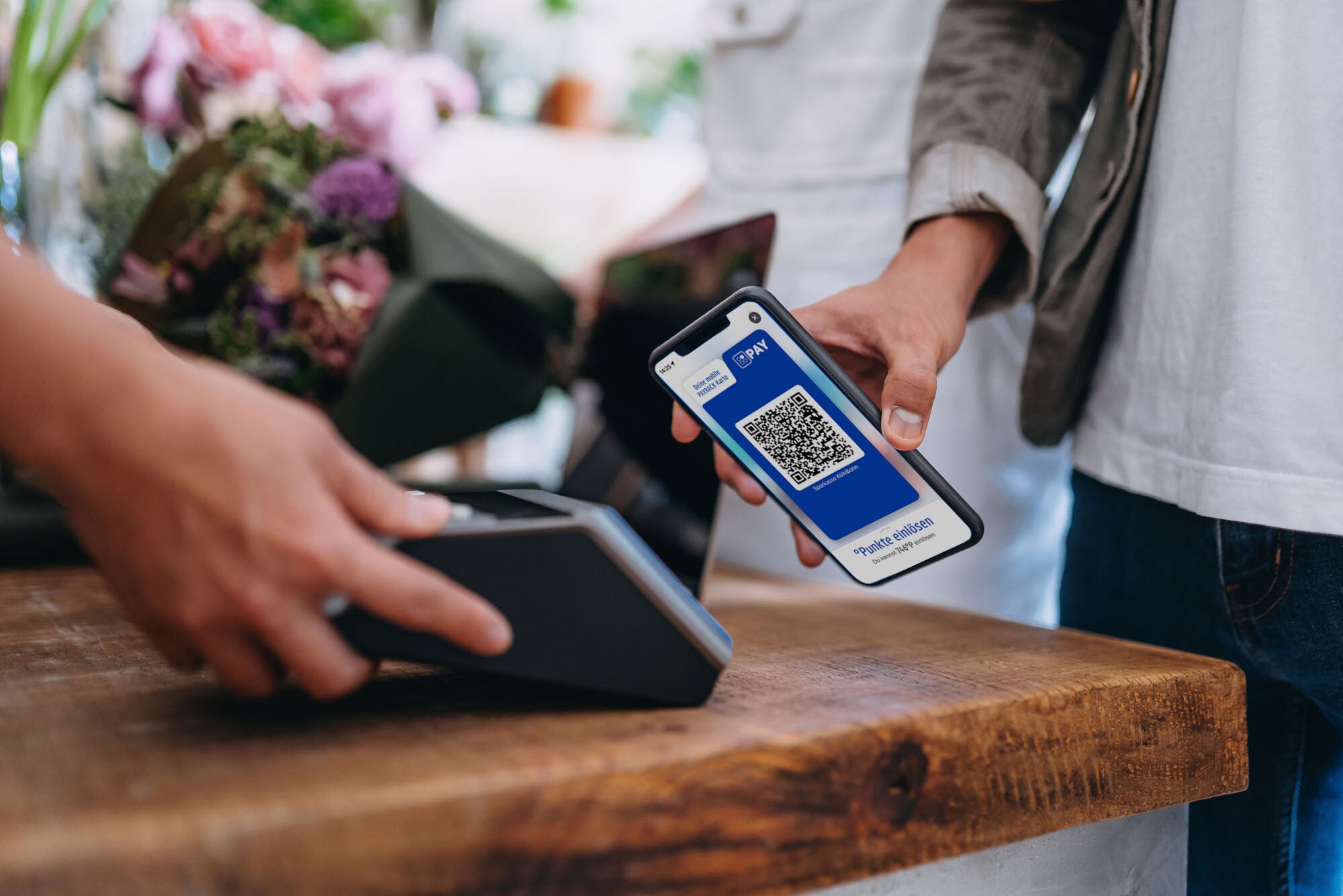 Eine Person bezahlt kontaktlos via Mobile Pay in einem Blumenladen mit einem QR-Code in der PAYBACK-App