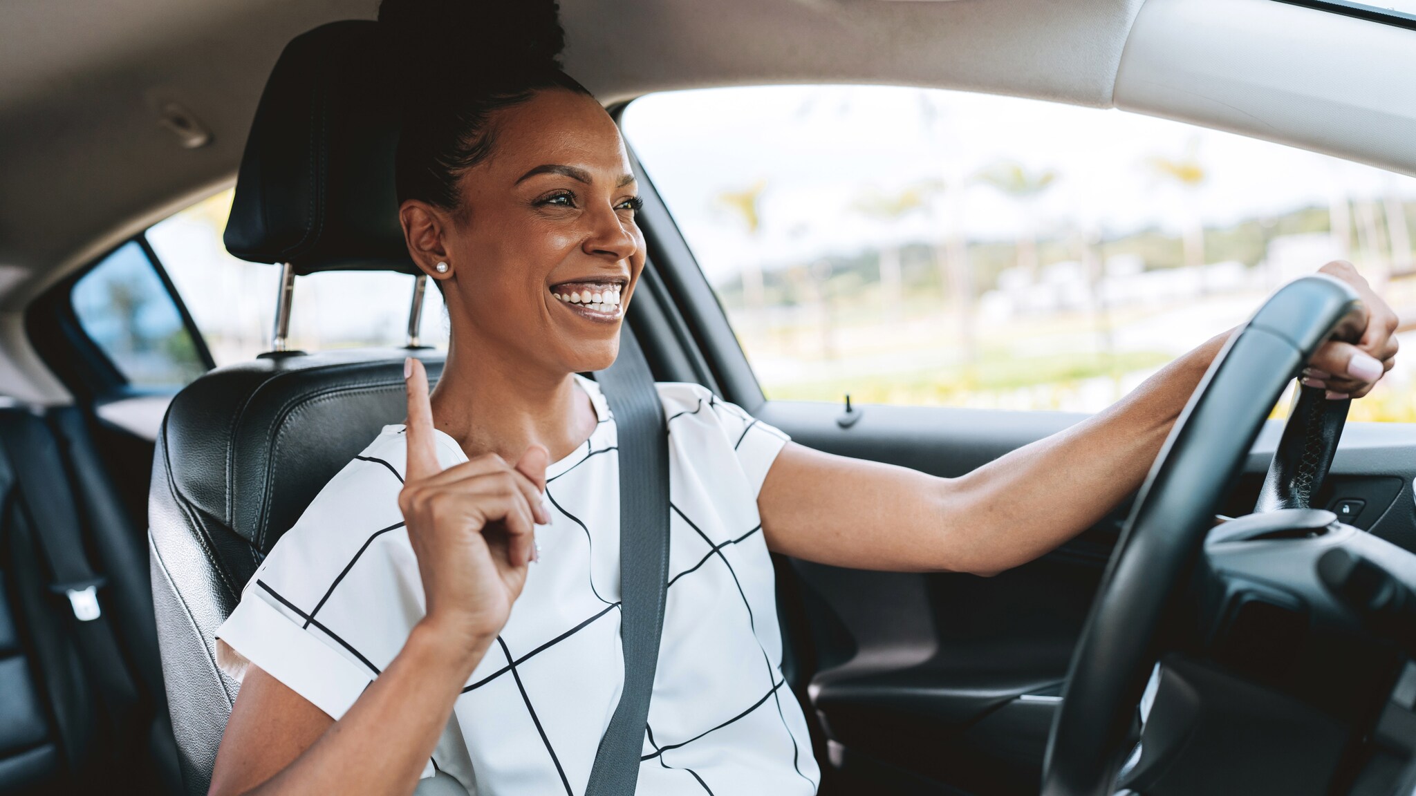 Eine lachende Frau im weißen Shirt am Steuer eines Autos mit einer Hand am Lenkrad. Eine lachende Frau im weißen Shirt am Steuer eines Autos mit einer Hand am Lenkrad.