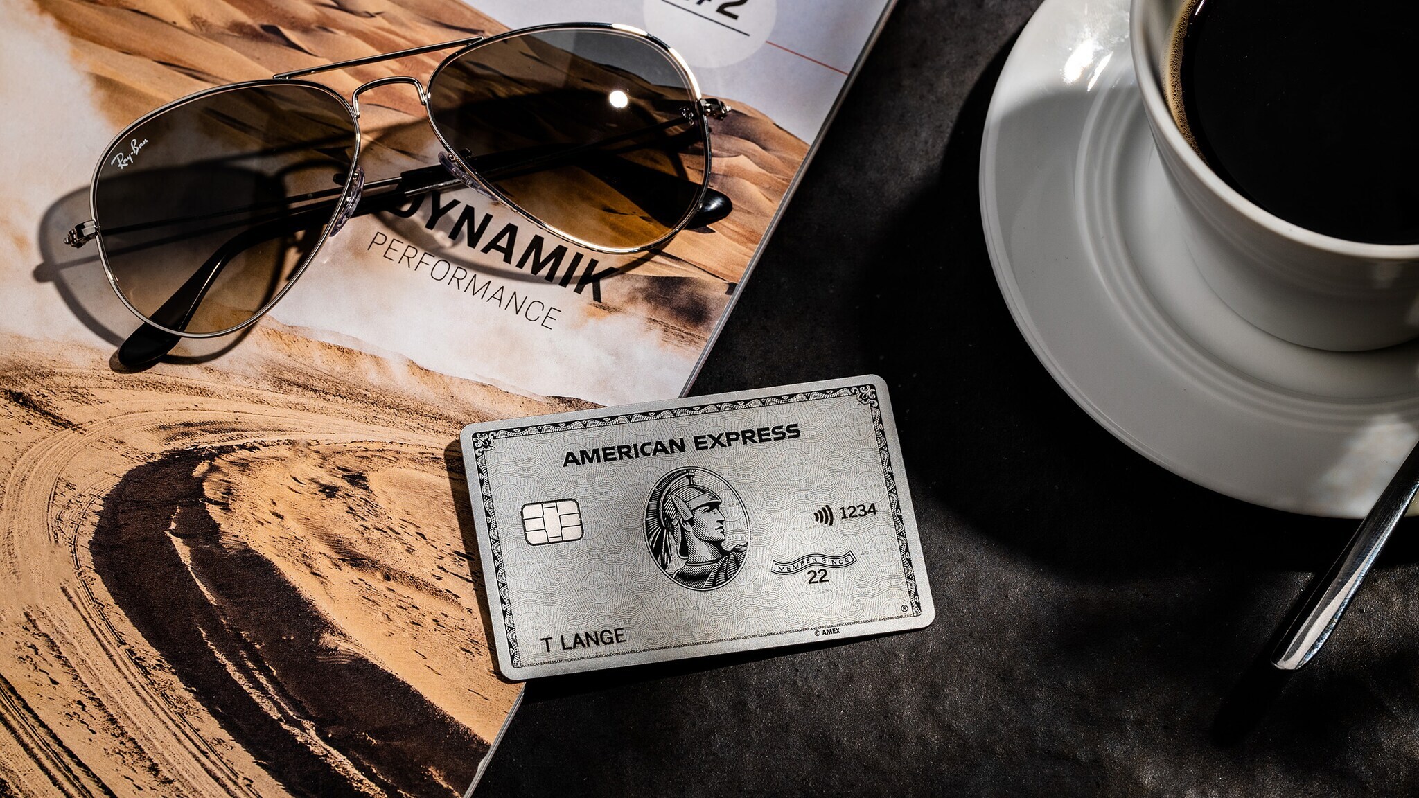 Eine Platinum Card von American Express liegt neben einer Kaffeetasse und einer Sonnenbrille.