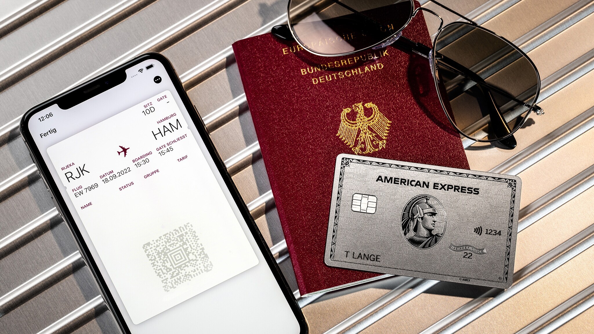 Eine American Express Platinum Card liegt auf einem Reisepass neben einer mobilen Bordkarte auf einem Smartphone.