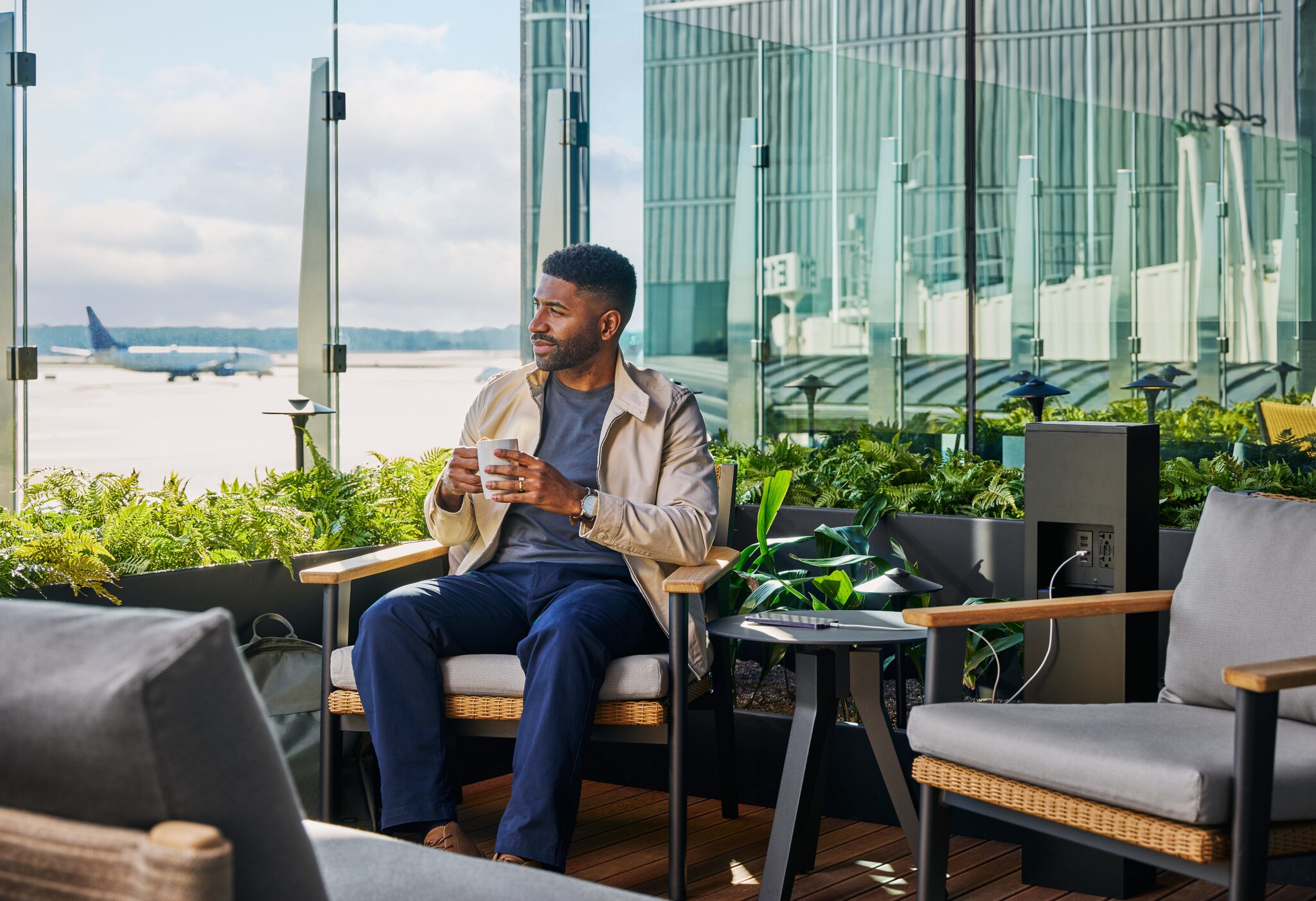 Ein Mann sitzt mit einer Kaffeetasse auf einer Terrasse mit Blick auf ein Flughafenrollfeld. Ein Mann sitzt mit einer Kaffeetasse auf einer Terrasse mit Blick auf ein Flughafenrollfeld.