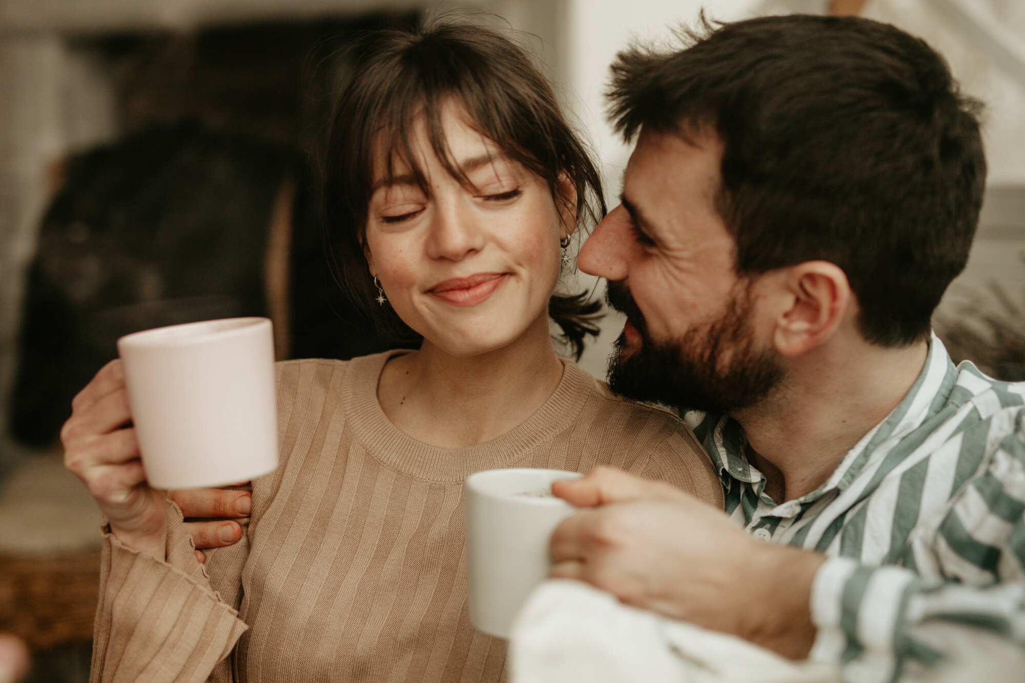 Nahaufnahme eines glücklichen, aneinander gekuschelten Paares mit Kaffeetassen Nahaufnahme eines glücklichen, aneinander gekuschelten Paares mit Kaffeetassen