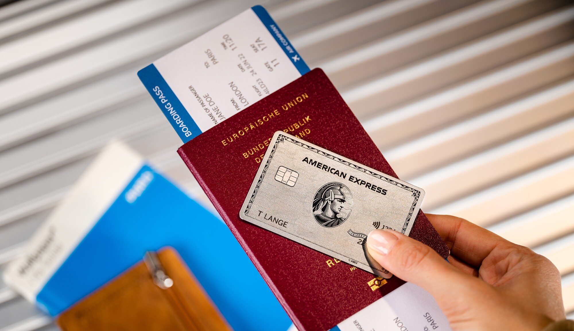 Eine Hand hält eine Platinum Kreditkarte von American Express auf einem Reisepass mit Bordkarte. Eine Hand hält eine Platinum Kreditkarte von American Express auf einem Reisepass mit Bordkarte.