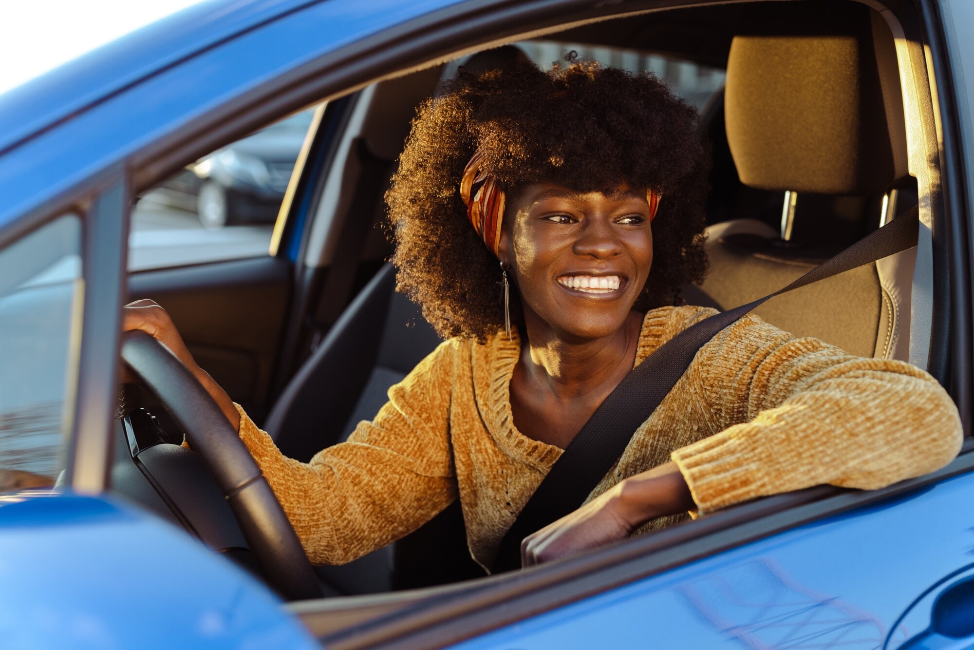 Eine lachende Frau am Steuer eines blauen Autos bei geöffnetem Fenster. Eine lachende Frau am Steuer eines blauen Autos bei geöffnetem Fenster.