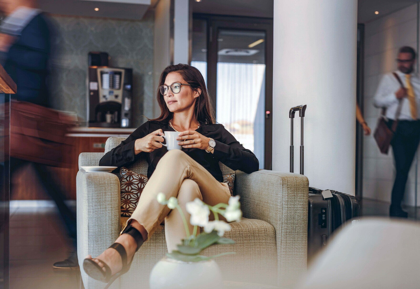 Eine Frau mit einer Kaffeetasse in der Hand sitzt entspannt in einer Airport-Lounge