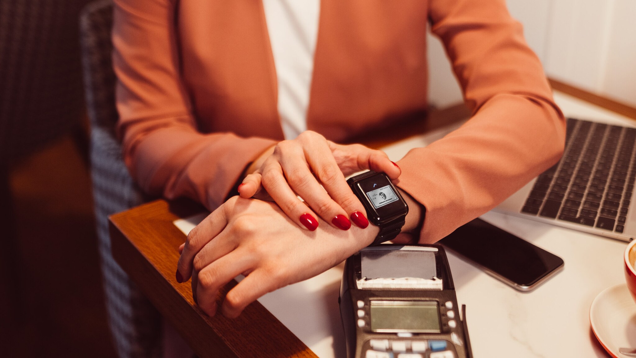 Eine Frau bezahlt mit einer American Express Kreditkarte via Apple Watch an einem Kartenlesegerät in einem Café Eine Frau bezahlt mit einer American Express Kreditkarte via Apple Watch an einem Kartenlesegerät in einem Café