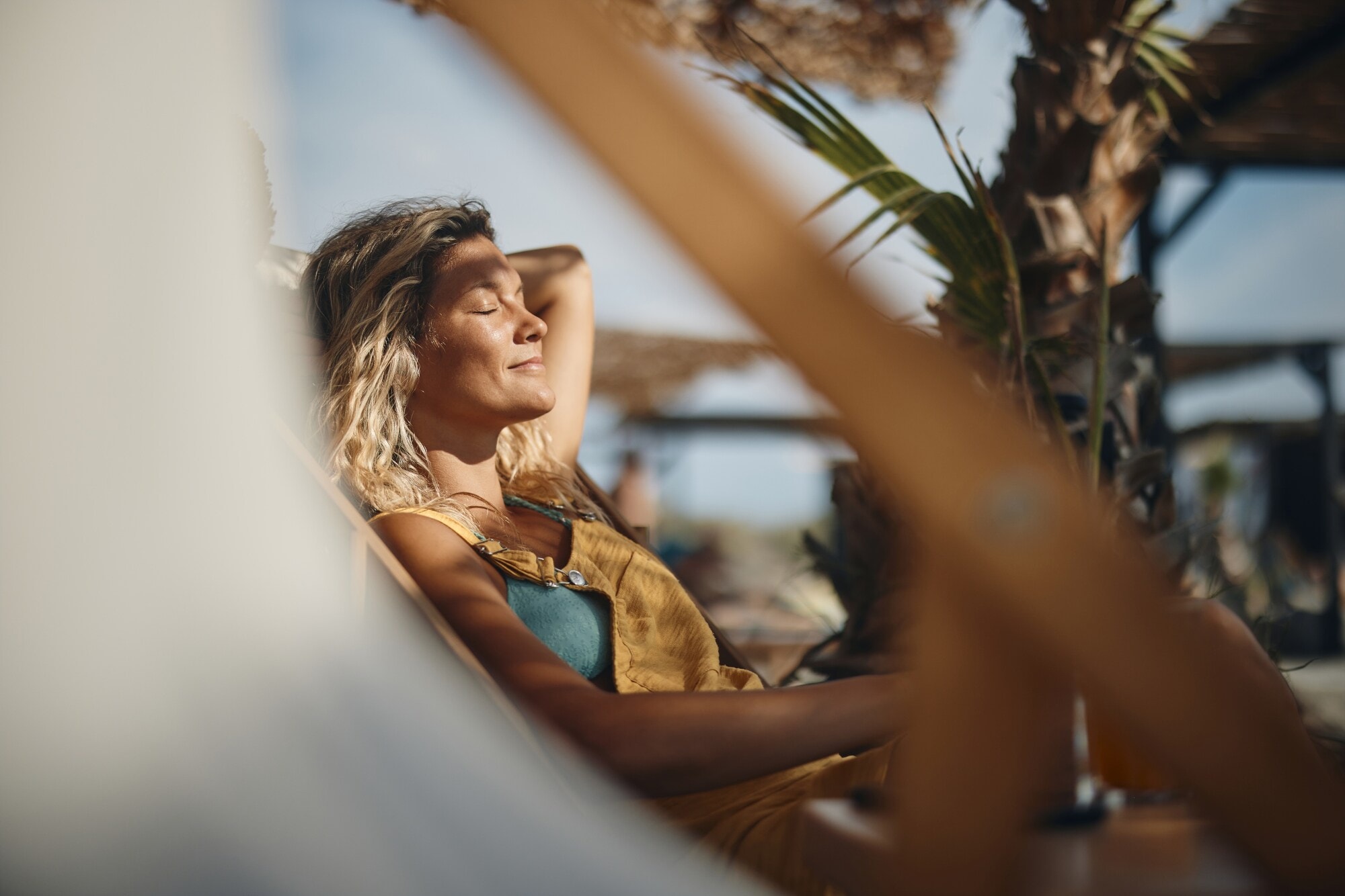 Nahaufnahme einer lächelnden Frau, die mit geschlossenen Augen die Sonne in einem Liegestuhl am Strand genießt Nahaufnahme einer lächelnden Frau, die mit geschlossenen Augen die Sonne in einem Liegestuhl am Strand genießt