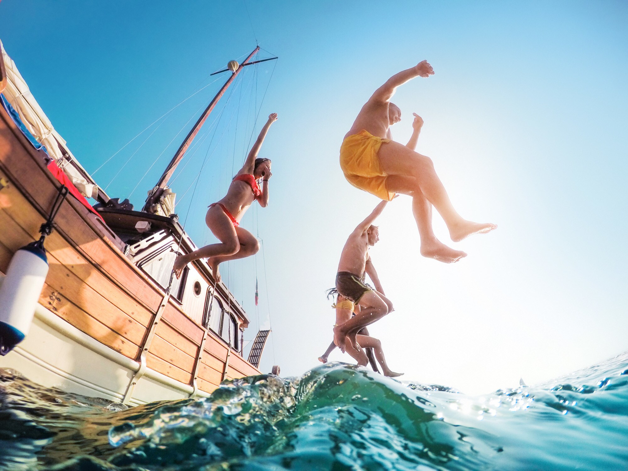 Untersicht einer Personengruppe, die in Badekleidung von einem Segelboot ins Wasser springt Untersicht einer Personengruppe, die in Badekleidung von einem Segelboot ins Wasser springt