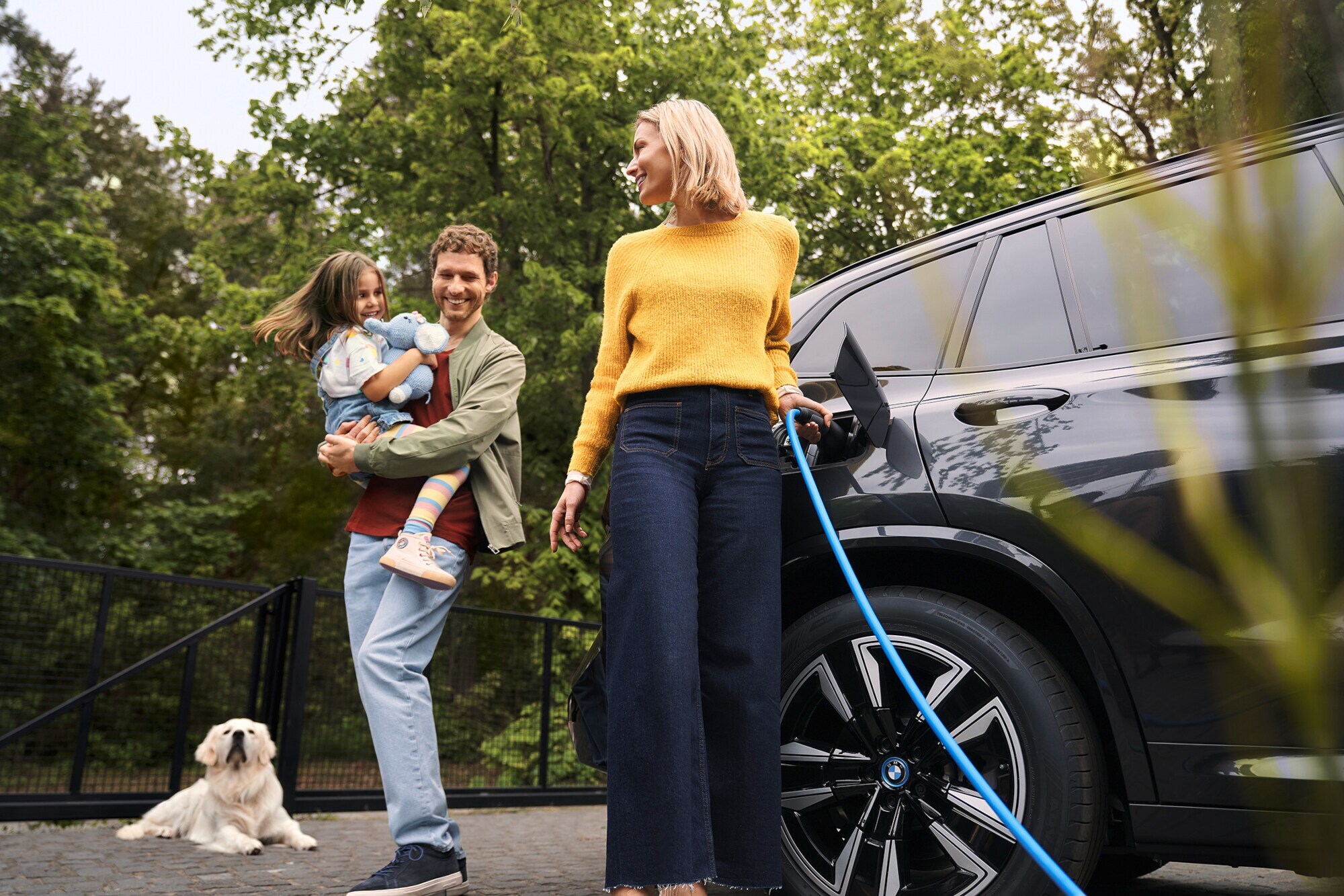 Eine glückliche Familie mit Kind und Hund beim Laden eines BMW-Elektroautos.