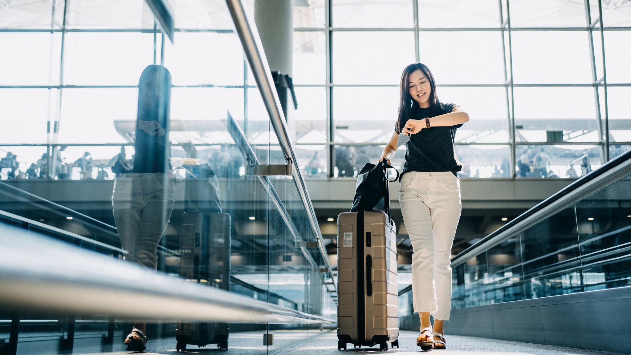 Eine Frau mit Rollkoffer schaut auf Ihre Armbanduhr in einem Flughafenterminal.