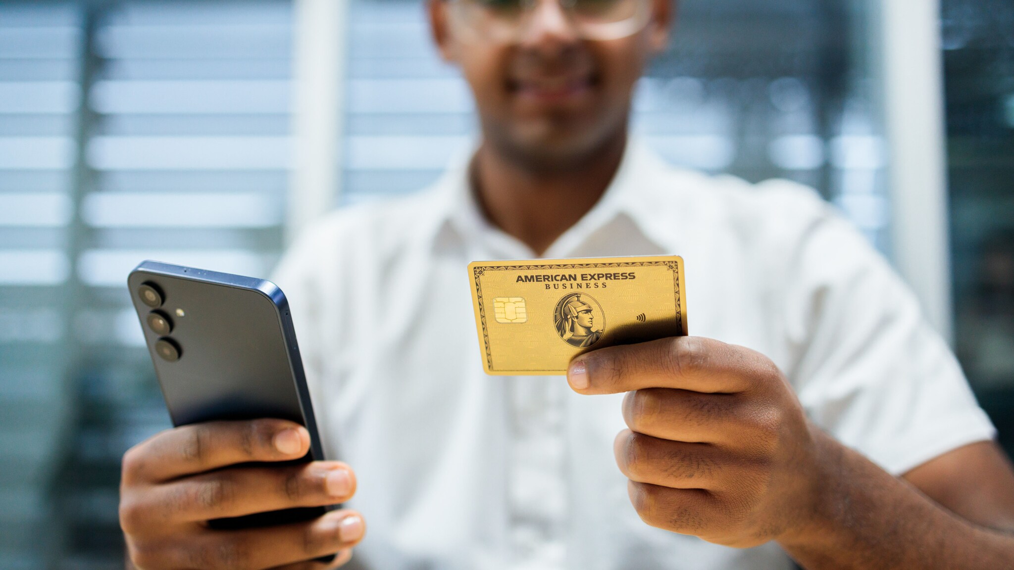 Eine Person hält in einer Hand ein Smartphone und in der anderen eine Business Gold Card von American Express. Eine Person hält in einer Hand ein Smartphone und in der anderen eine Business Gold Card von American Express.