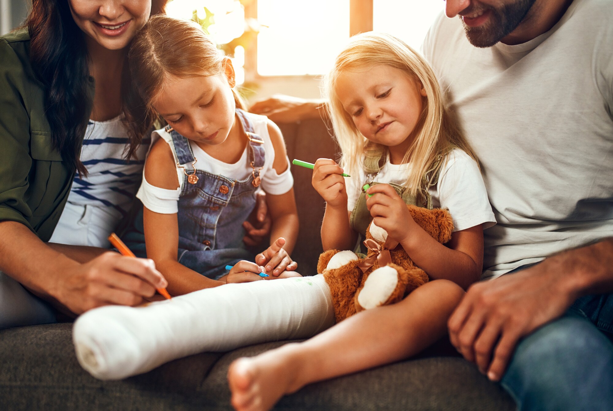Zwei Erwachsene auf einem Sofa mit zwei Mädchen, von denen eine ein eingegipstes Bein hat