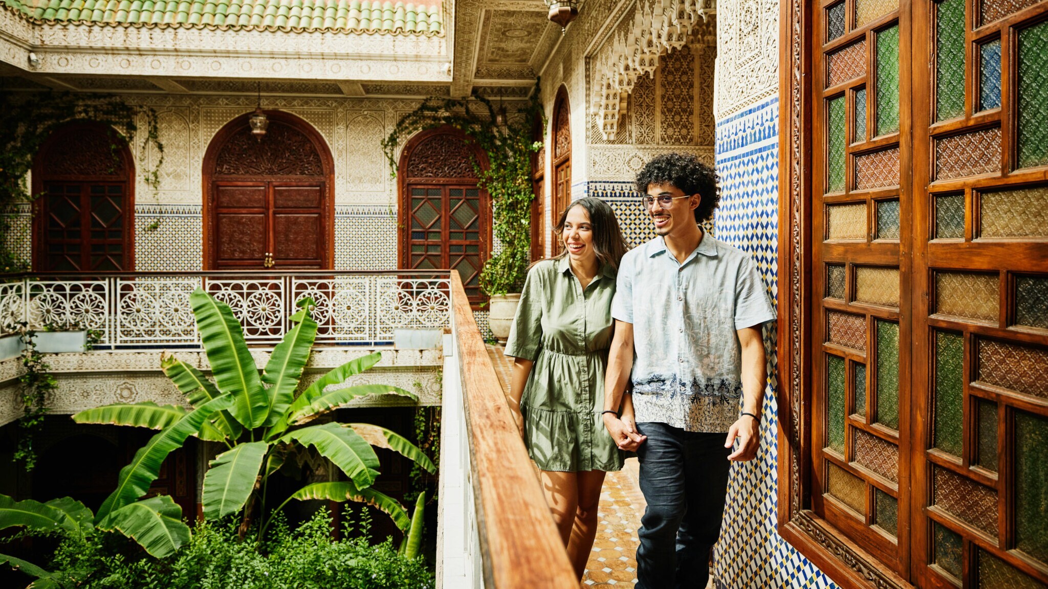 Ein junges Paar läuft auf einem Balkon in einem begrünten Innenhof eines marokkanischen Hotels.
