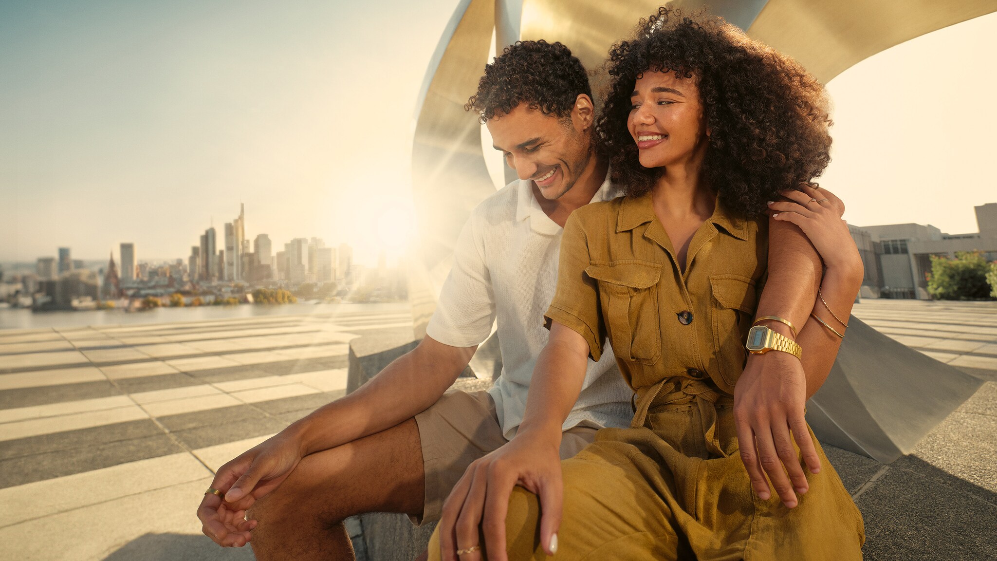 Mann und Frau sitzen Arm in Arm draußen vor einem modernen Kunstwerk. Mann und Frau sitzen Arm in Arm draußen vor einem modernen Kunstwerk.