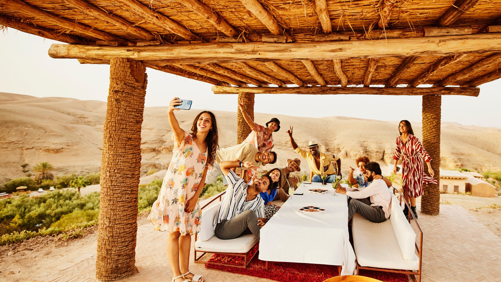 Eine Frau macht ein Selfie vor einer Personengruppe an einem Tisch in einem Wüstencamp. Eine Frau macht ein Selfie vor einer Personengruppe an einem Tisch in einem Wüstencamp.