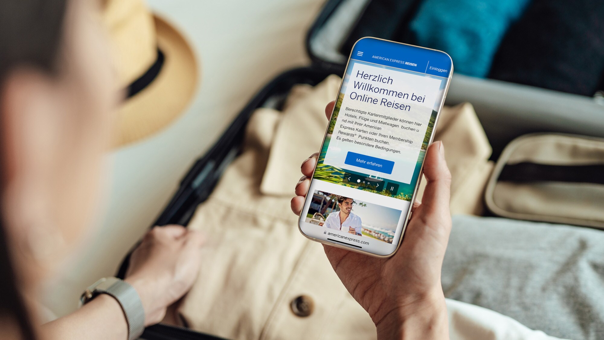 Eine Person hält ein Smartphone mit dem Online-Reiseservice von American Express auf dem Display über einen gepackten Koffer.