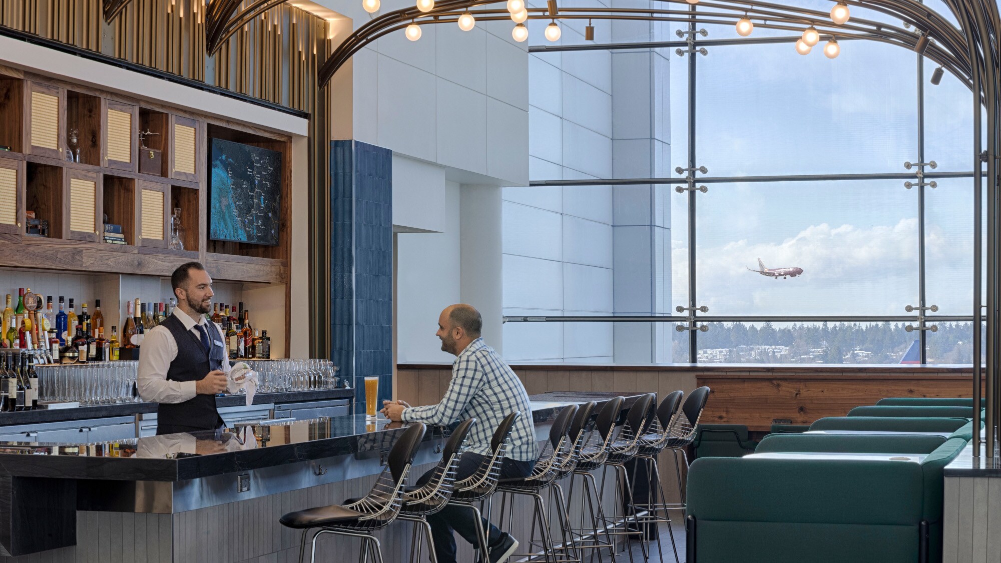 Ein Mann sitzt an der Bar einer modernen Flughafen-Lounge mit Blick aufs Rollfeld. Ein Mann sitzt an der Bar einer modernen Flughafen-Lounge mit Blick aufs Rollfeld.