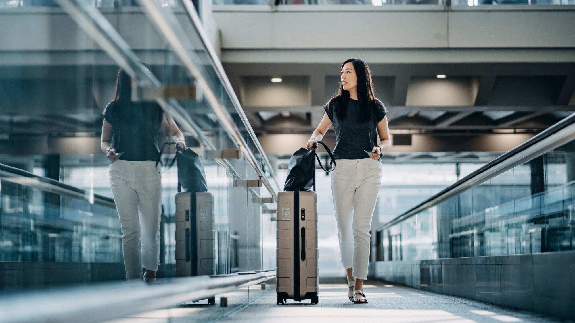 Eine elegante, junge Frau läuft mit einem Rollkoffer durch eine Eingangshalle am Flughafen Eine elegante, junge Frau läuft mit einem Rollkoffer durch eine Eingangshalle am Flughafen