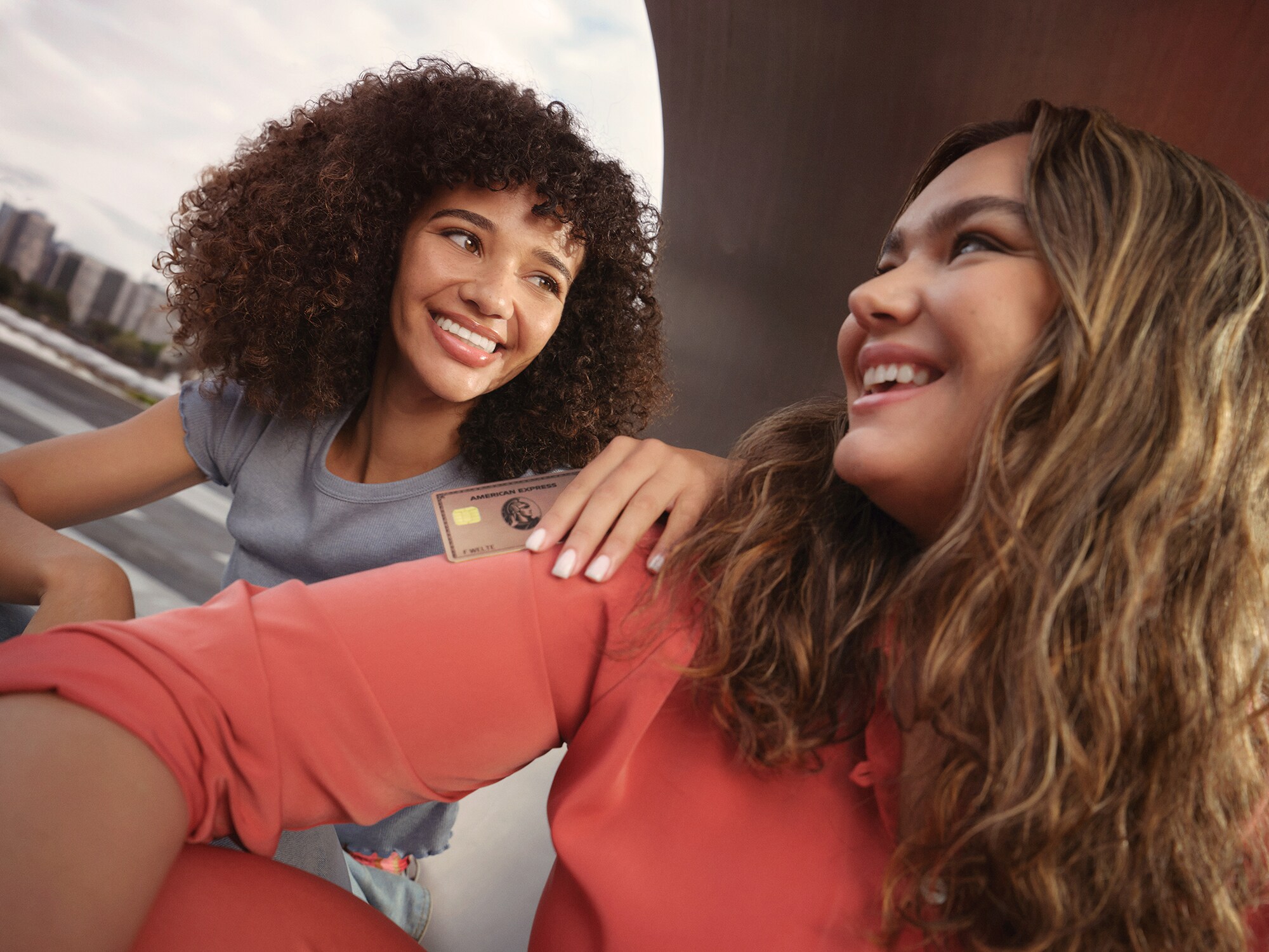 Zwei Frauen schauen sich lächelnd an, die hintere Frau hält die Gold Card in Rosé-Metall in der Hand.