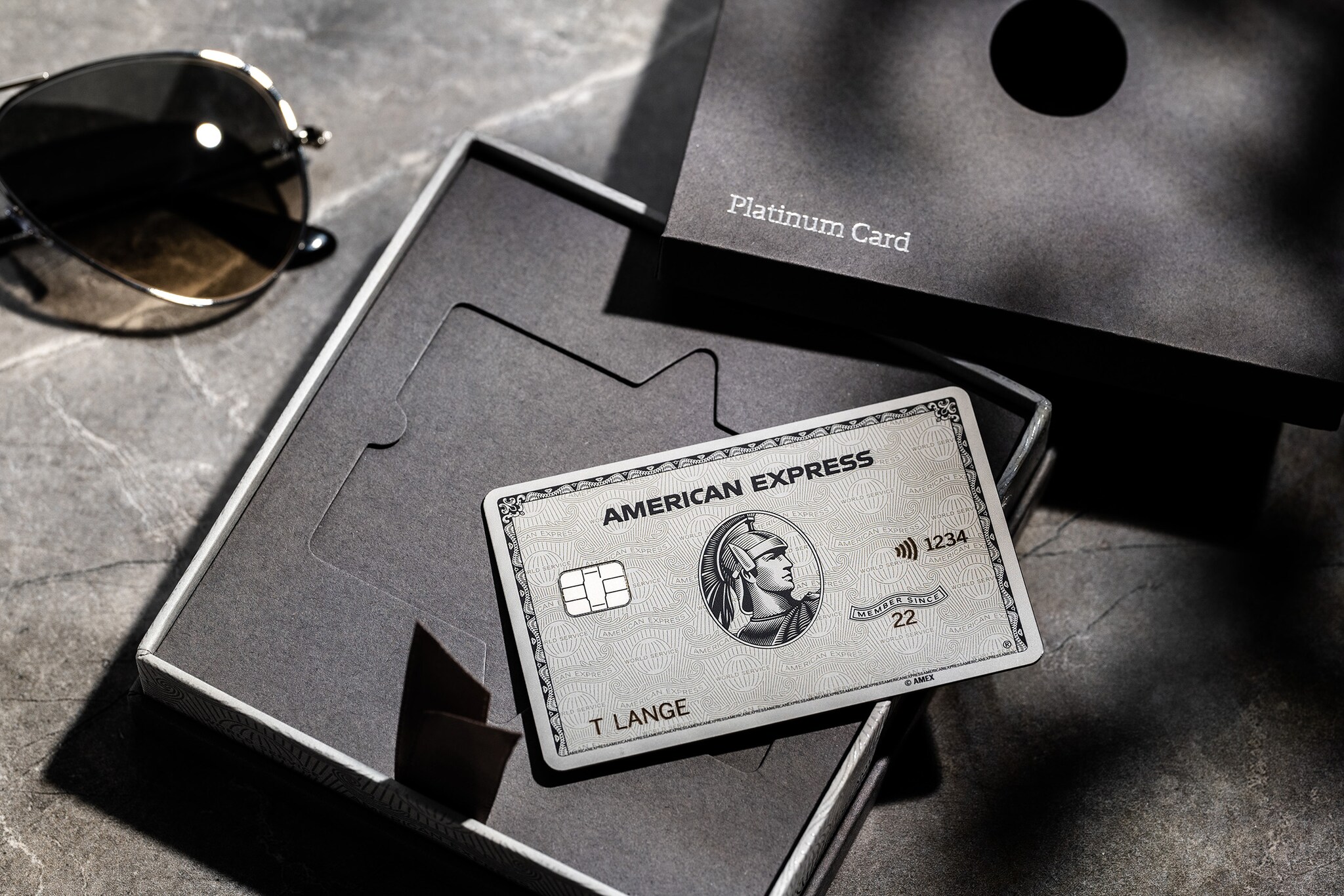 Eine American Express Platinum Card aus Metall liegt auf einer geöffneten Präsentationsbox aus grauer Feinkartonage mit Platinum Card Aufschrift auf einem Marmortisch