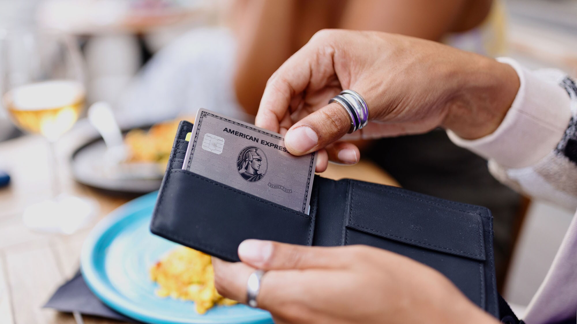 Nahaufnahme einer Hand, die beim Lunch eine silberne American Express Kreditkarte aus einem Portemonnaie zieht.