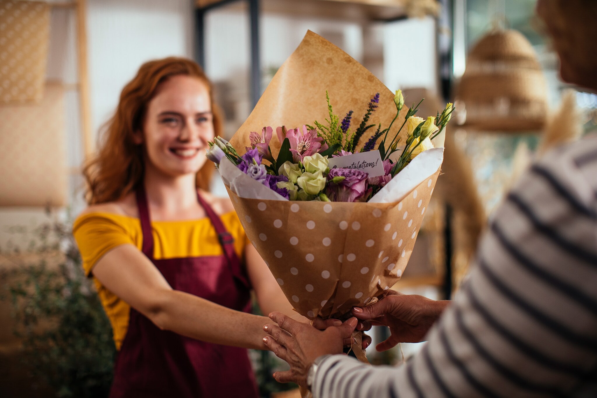 Eine junge Verkäuferin überreicht einem Kunden einen Blumenstrauß in einem Geschäft. Eine junge Verkäuferin überreicht einem Kunden einen Blumenstrauß in einem Geschäft.