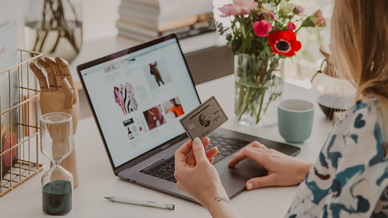 Eine Platinum Kreditkarte von American Express in der Hand einer Frau beim Onlineshopping an einem Laptop auf einem Schreibtisch. Eine Platinum Kreditkarte von American Express in der Hand einer Frau beim Onlineshopping an einem Laptop auf einem Schreibtisch.