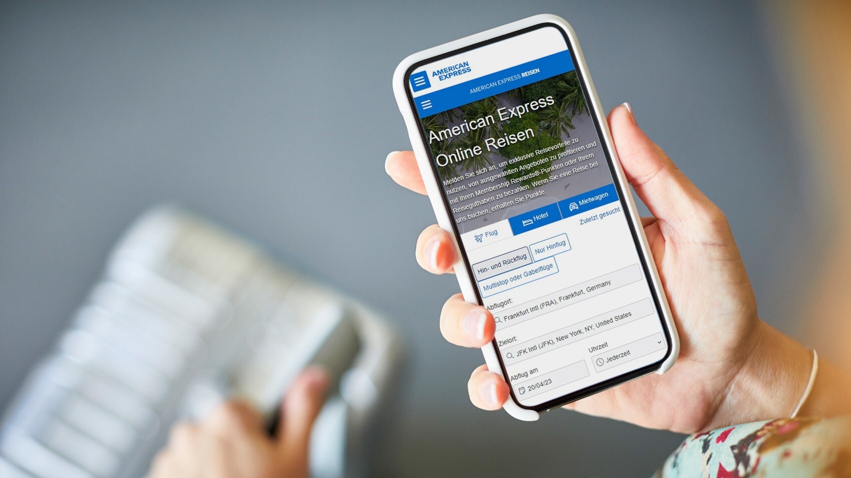 Ein Smartphone mit dem American Express Online-Reiseportal auf dem Display wird von einer Hand über einen Koffer gehalten. Ein Smartphone mit dem American Express Online-Reiseportal auf dem Display wird von einer Hand über einen Koffer gehalten.