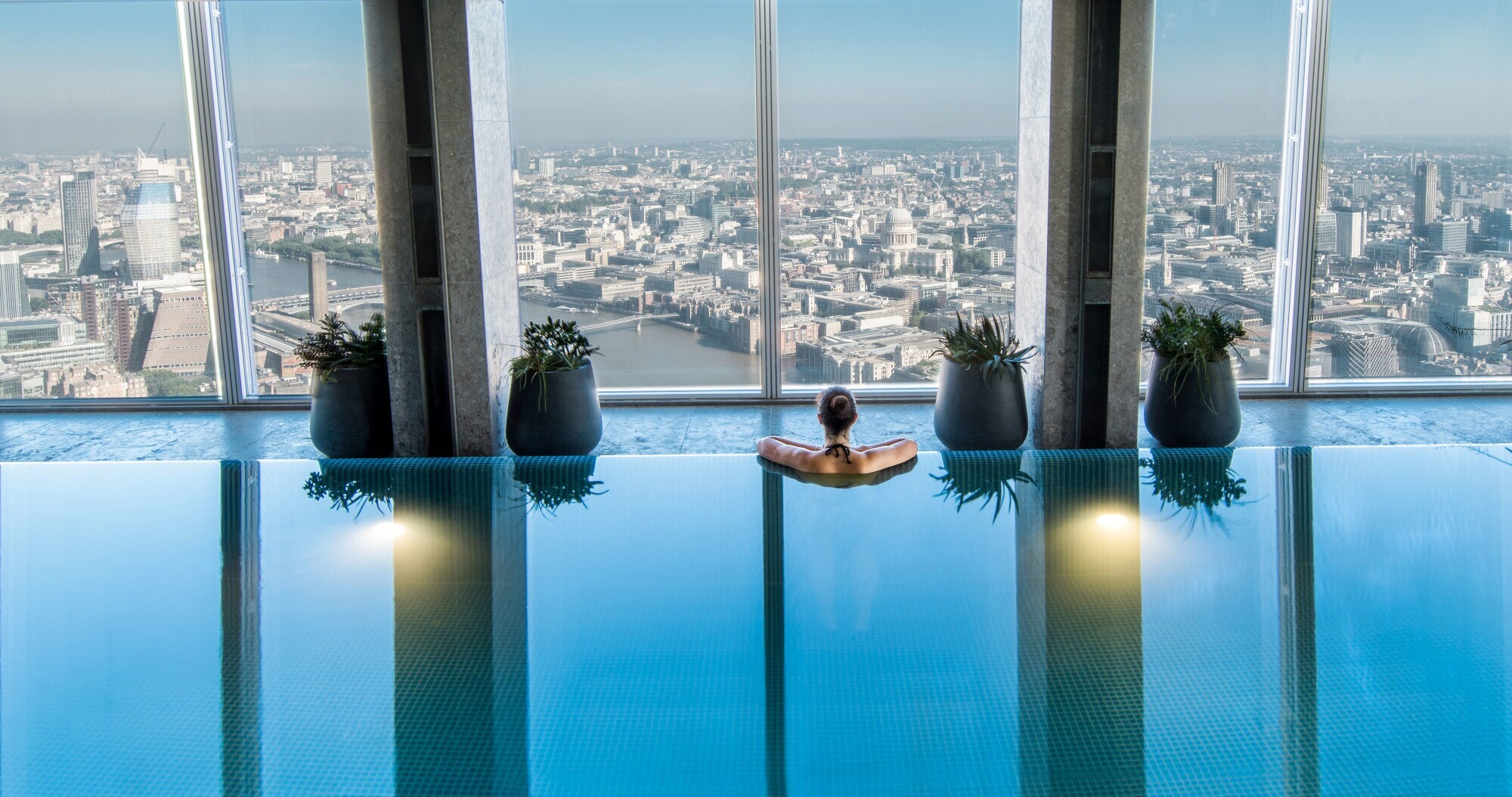 Rückansicht einer Frau in einem Pool im oberen Stockwerk eines Wolkenkratzers mit Ausblick auf die Skyline von London. Rückansicht einer Frau in einem Pool im oberen Stockwerk eines Wolkenkratzers mit Ausblick auf die Skyline von London.