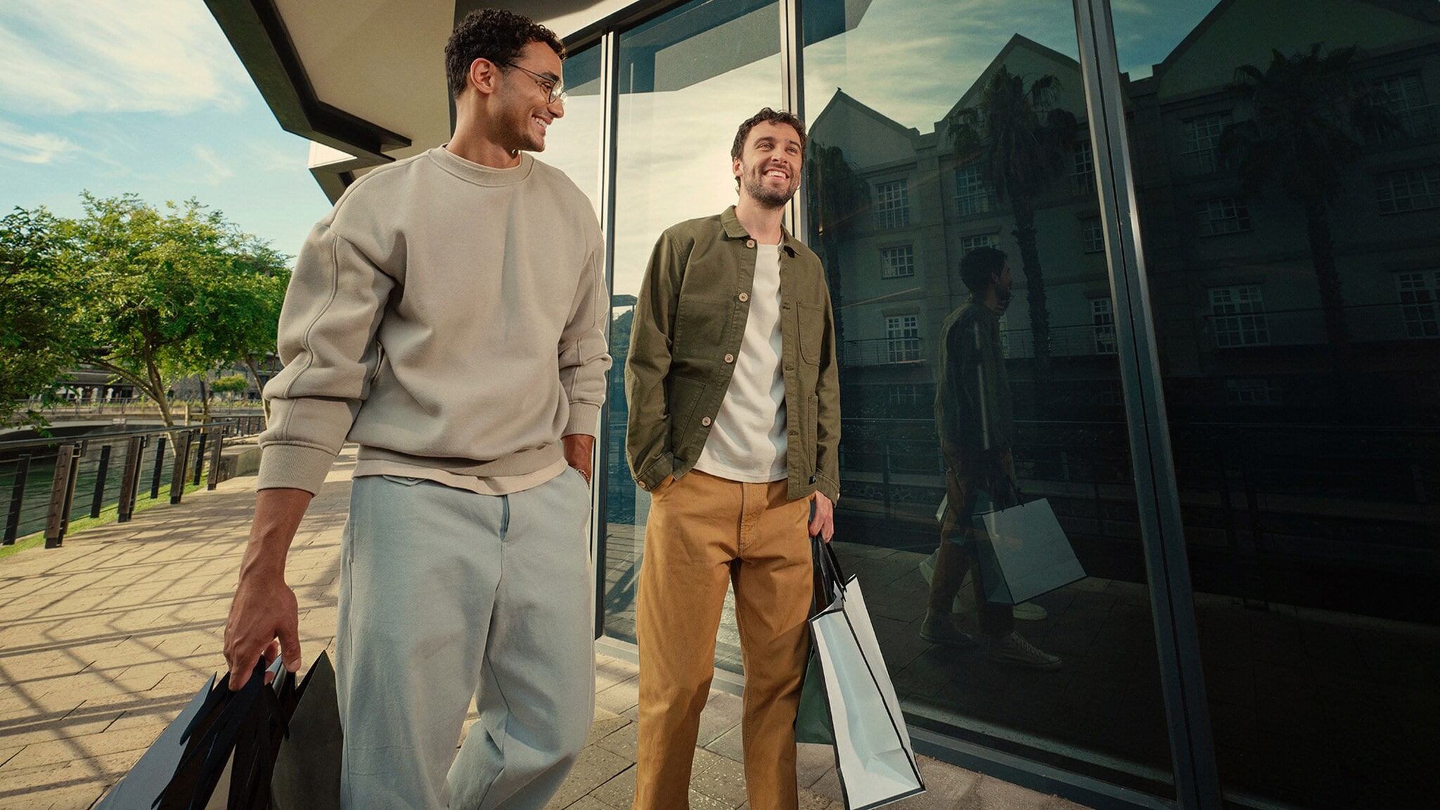 Zwei junge Männer spazieren vor einem Geschäft, beide haben hochwertige Einkaufstüten aus Papier in der Hand. Zwei junge Männer spazieren vor einem Geschäft, beide haben hochwertige Einkaufstüten aus Papier in der Hand.