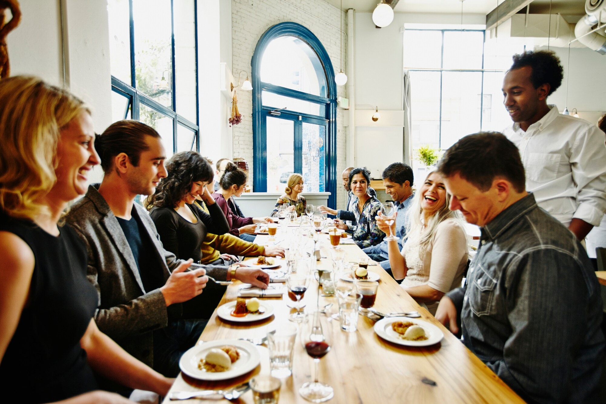 Eine Personengruppe sitzt beim Essen an einem langen Holztisch in einem kleinen Restaurant. Eine Personengruppe sitzt beim Essen an einem langen Holztisch in einem kleinen Restaurant.