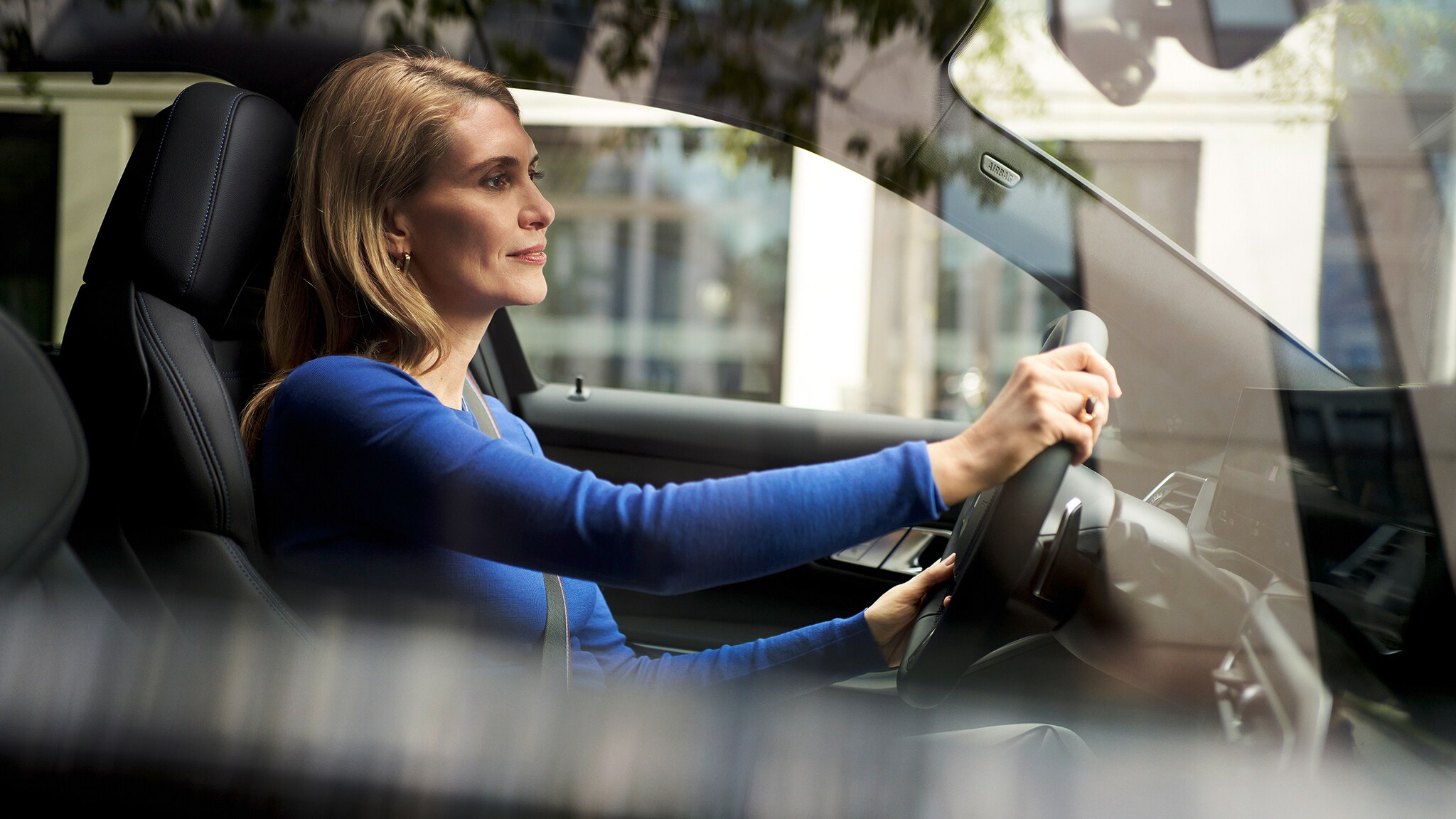 Eine Frau mit blauem Oberteil am Steuer eines BMW auf der Straße.