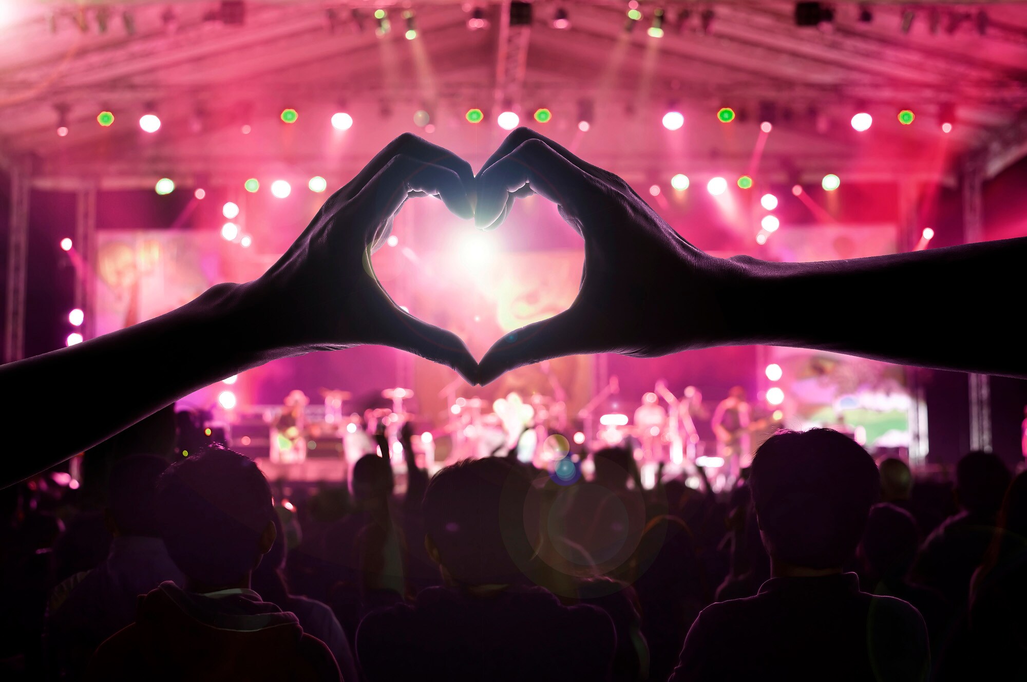 Zwei Hände formen ein Herz im Publikum vor einer Konzertbühne.