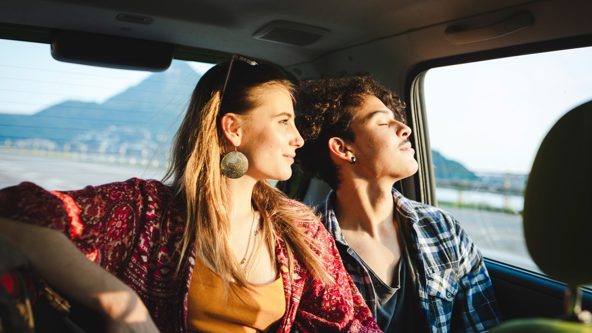 Ein junges Paar auf dem Rücksitz eines Autos blickt aus dem Fenster bei warmem Sonnenlicht. Ein junges Paar auf dem Rücksitz eines Autos blickt aus dem Fenster bei warmem Sonnenlicht.