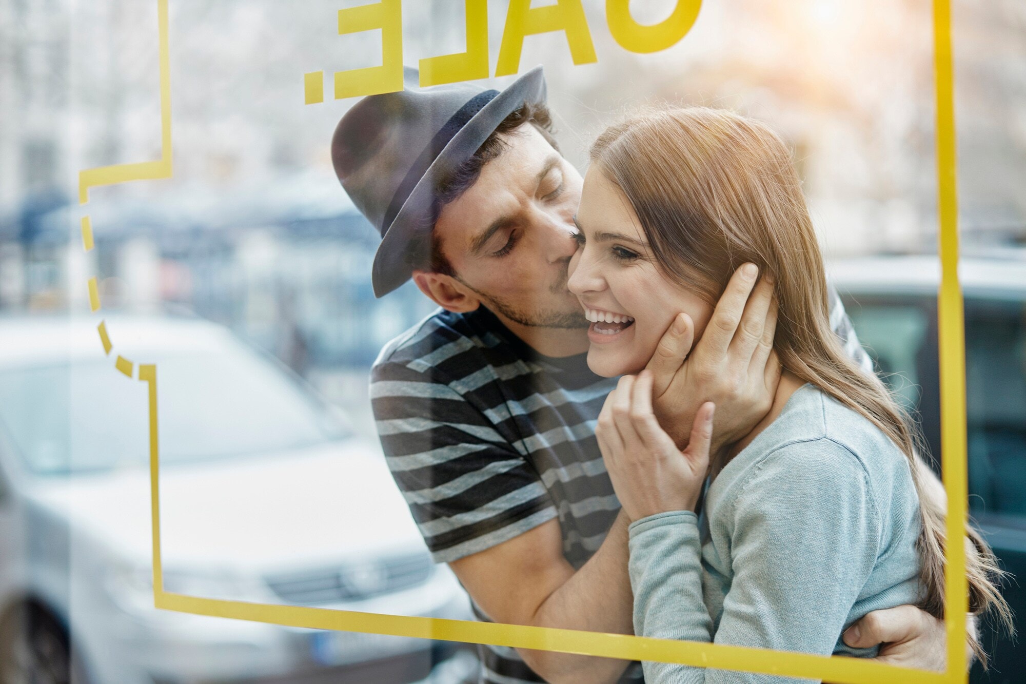 Ein junges Paar steht auf der Straße vor dem Fenster eines Cafés und umarmt sich glücklich Ein junges Paar steht auf der Straße vor dem Fenster eines Cafés und umarmt sich glücklich