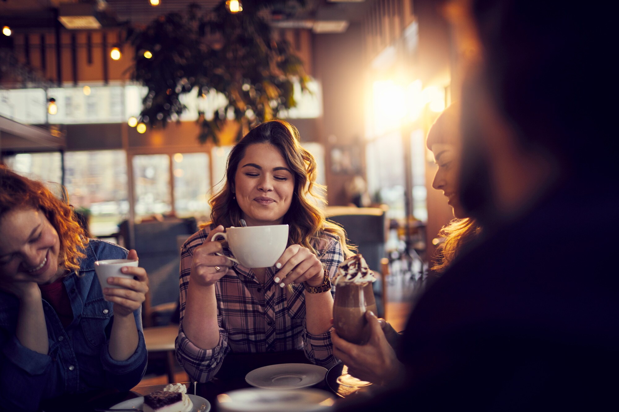 Eine junge Studentin genießt eine Tasse Kaffee in Gesellschaft ihrer Freunde in einem Café Eine junge Studentin genießt eine Tasse Kaffee in Gesellschaft ihrer Freunde in einem Café