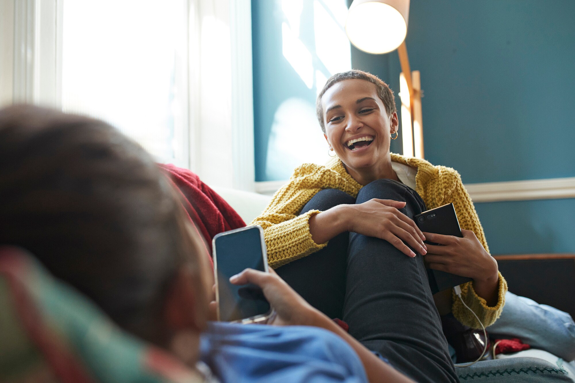 Zwei junge, vertraute Menschen mit Smartphones in den Händen genießen lachend die gemeinsame Zeit auf einem Sofa Zwei junge, vertraute Menschen mit Smartphones in den Händen genießen lachend die gemeinsame Zeit auf einem Sofa