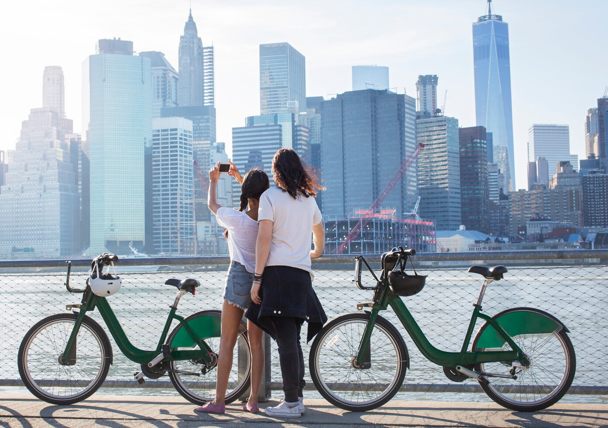 Rückansicht eines jungen, coolen Paares mit Fahrrädern, das auf die Skyline von Manhattan blickt Rückansicht eines jungen, coolen Paares mit Fahrrädern, das auf die Skyline von Manhattan blickt