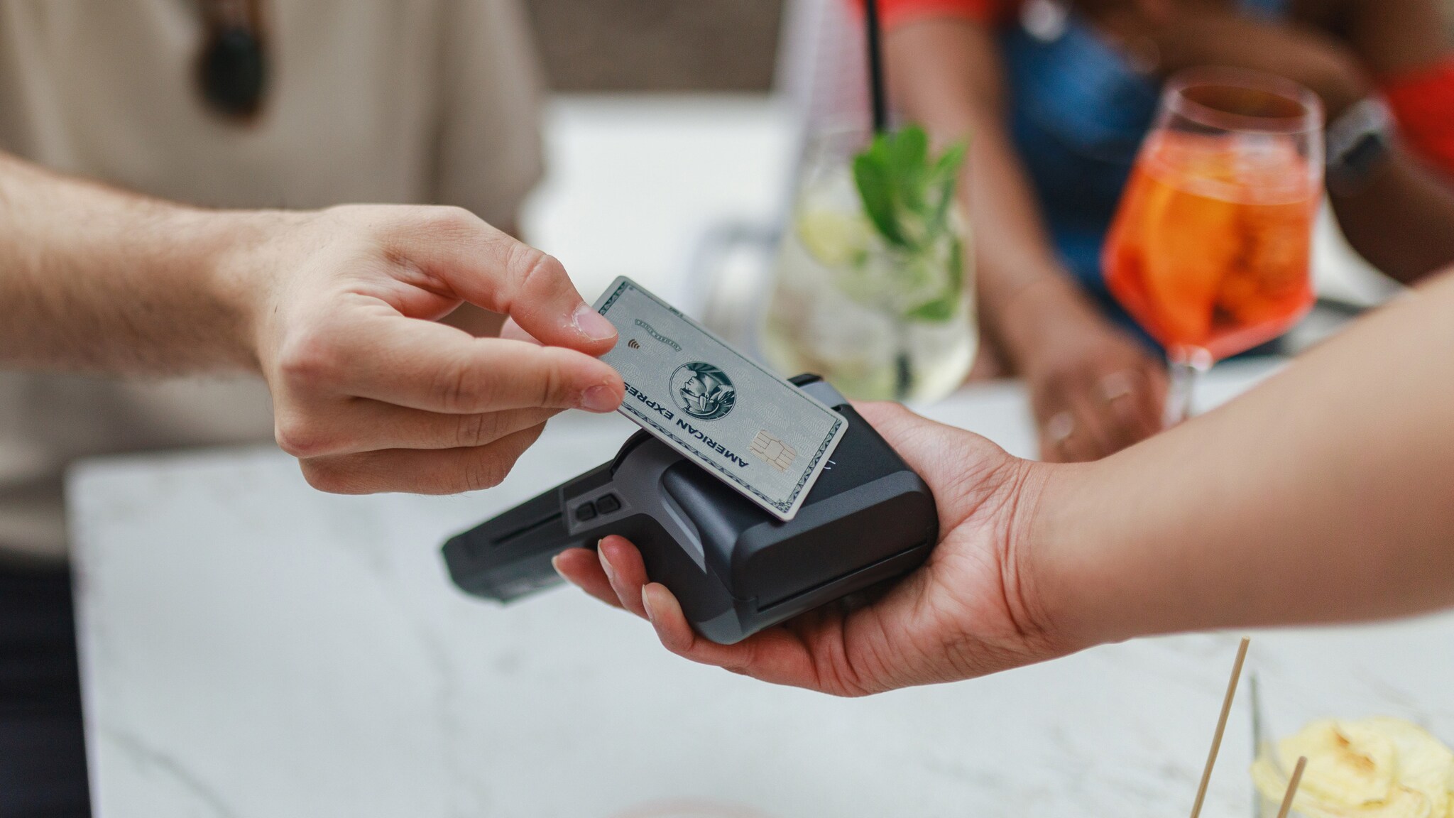 Kontaktlose Zahlung mit einer silbernen American Express Platinum Card an einem Kartenlesegerät in einem Restaurant.