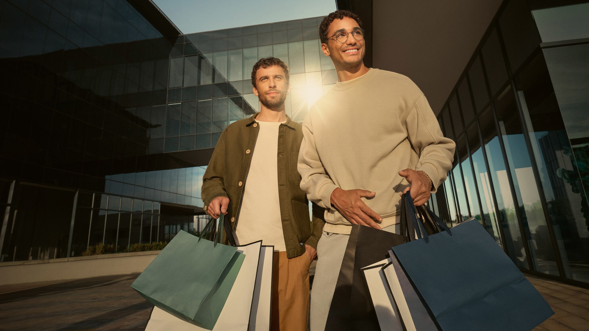 Zwei junge Männer mit Einkaufstüten in urbanem Setting bei Sonnenschein. Zwei junge Männer mit Einkaufstüten in urbanem Setting bei Sonnenschein.
