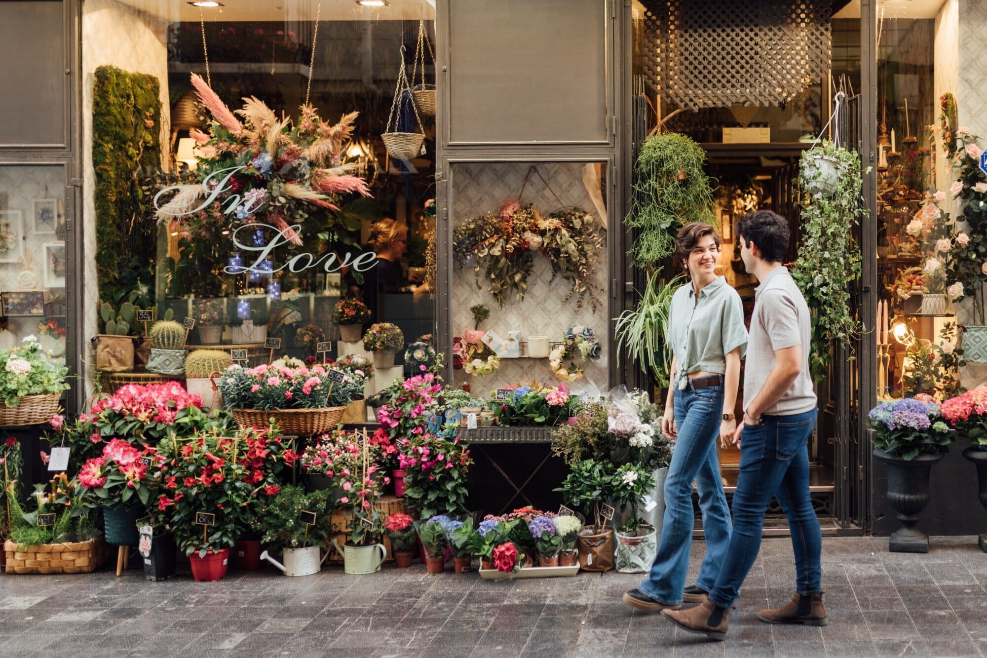 Ein Paar geht auf der Straße an einem üppig dekorierten Blumenladen vorbei. Ein Paar geht auf der Straße an einem üppig dekorierten Blumenladen vorbei.