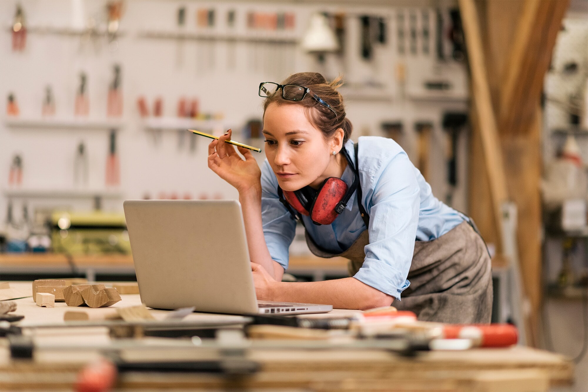 E-Rechnung 2025: Was Unternehmen jetzt tun und wissen müssen Eine Handwerkerin steht an einer Werkbank und blickt auf den vor ihr geöffneten Laptop.
