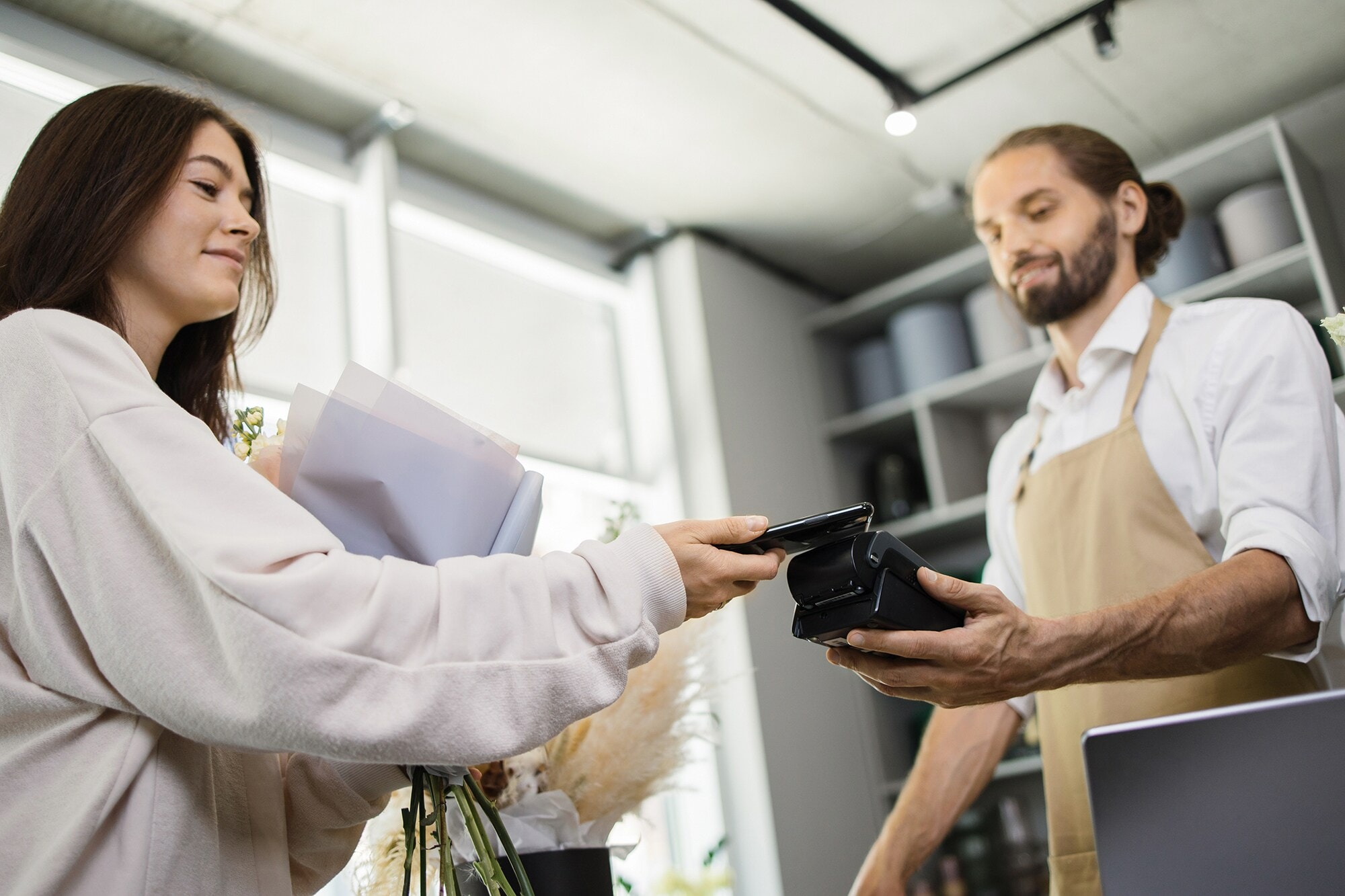 Kontaktloses bezahlen: mit Amex Business Cards & Google Pay™ Eine junge Frau bezahlt mit ihrem Smartphone im Blumenladen.