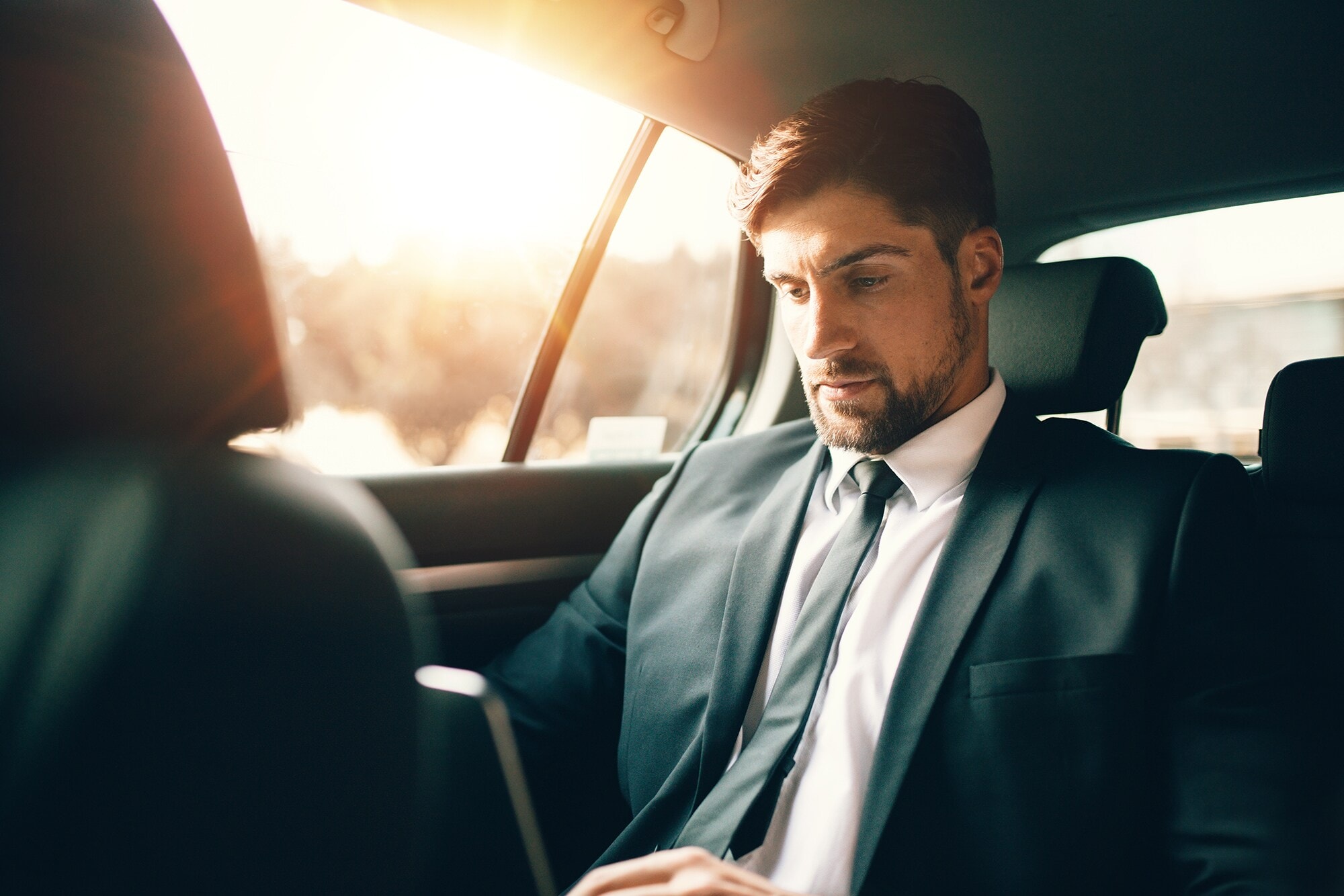 200 Euro SIXT ride Fahrtguthaben – mit American Express Ein Geschäftsmann sitzt mit Laptop auf dem Rücksitz eines Autos.