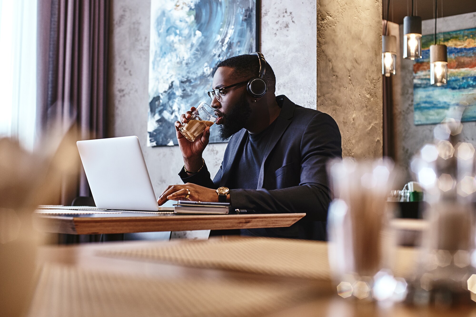 Ein Geschäftsmann mit Kopfhörer arbeitet in einer Hotellobby am Laptop.