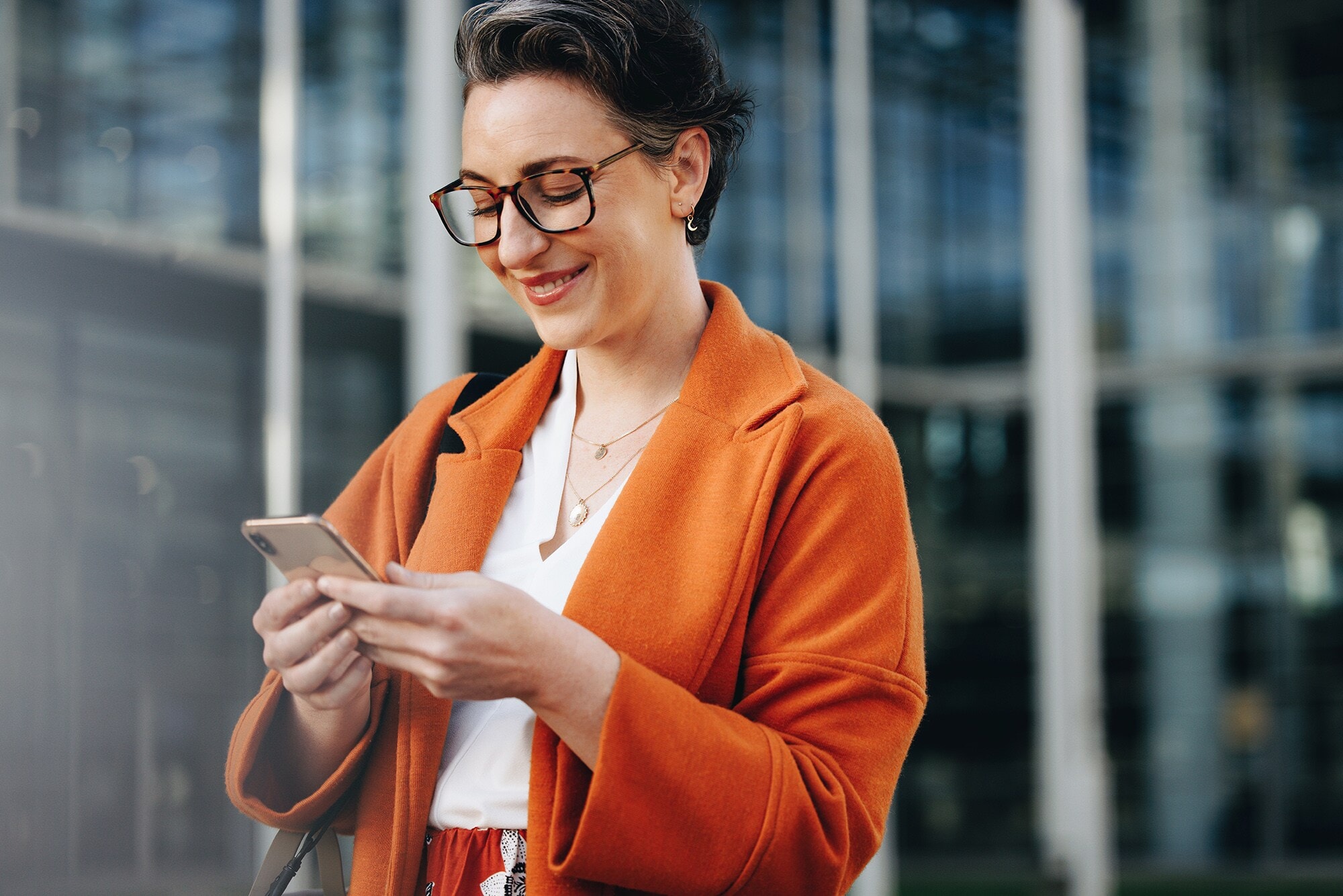 Amex Business Cards Geschäftspartnern empfehlen und belohnt werden Eine elegante Geschäftsfrau schaut auf ihr Smartphone.