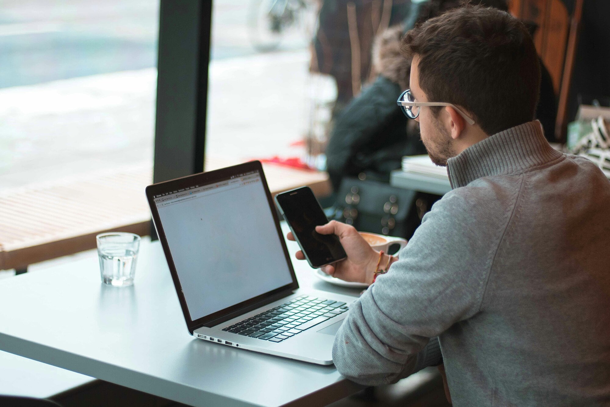 Amex Express List: Online zahlen, Kredibilität erhöhen, Wachstum fördern Ein Mann sitzt mit Laptop und im Cafe und schaut auf sein Smartphone.