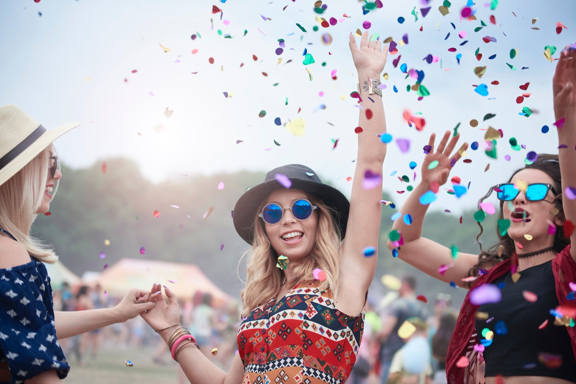 Drei junge, stylishe Frauen feiern auf einem Festival im Konfettiregen Drei junge, stylishe Frauen feiern auf einem Festival im Konfettiregen
