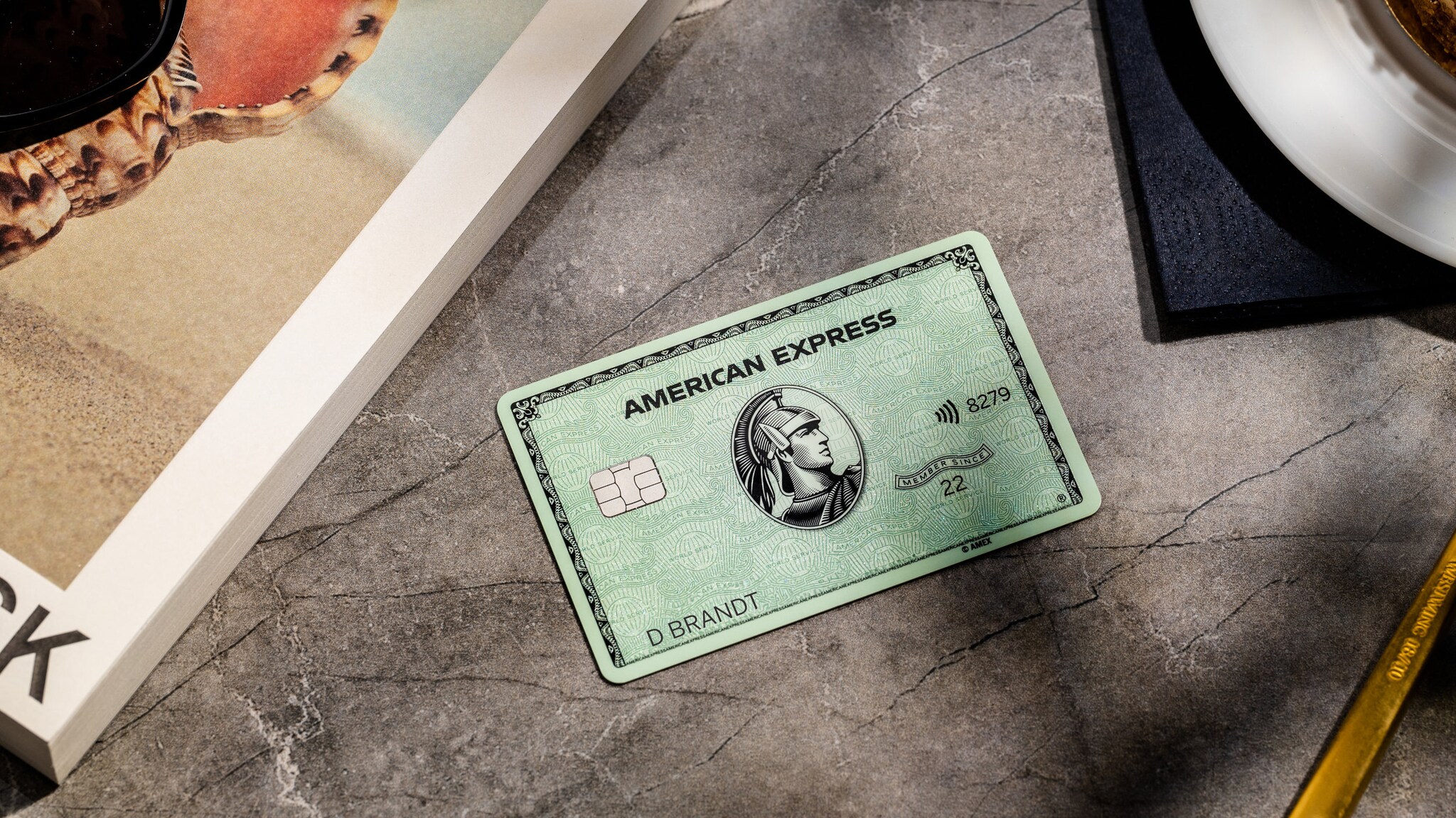 ine grüne American Express Kreditkarte liegt auf einem grauen Marmortisch neben einem Buch. ine grüne American Express Kreditkarte liegt auf einem grauen Marmortisch neben einem Buch.