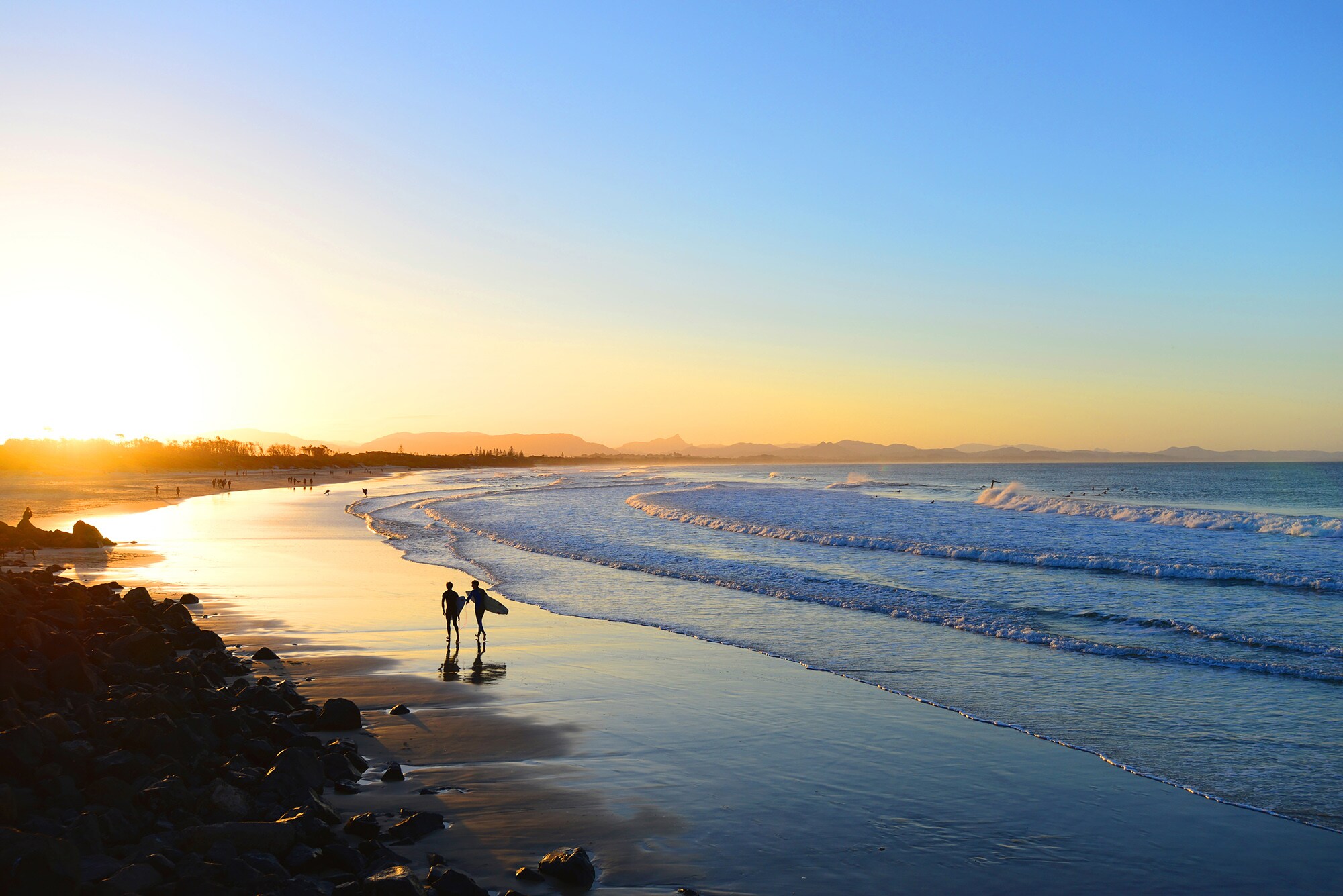Ein Sandstrand im Ausland mit Surfern bei Sonnenuntergang
